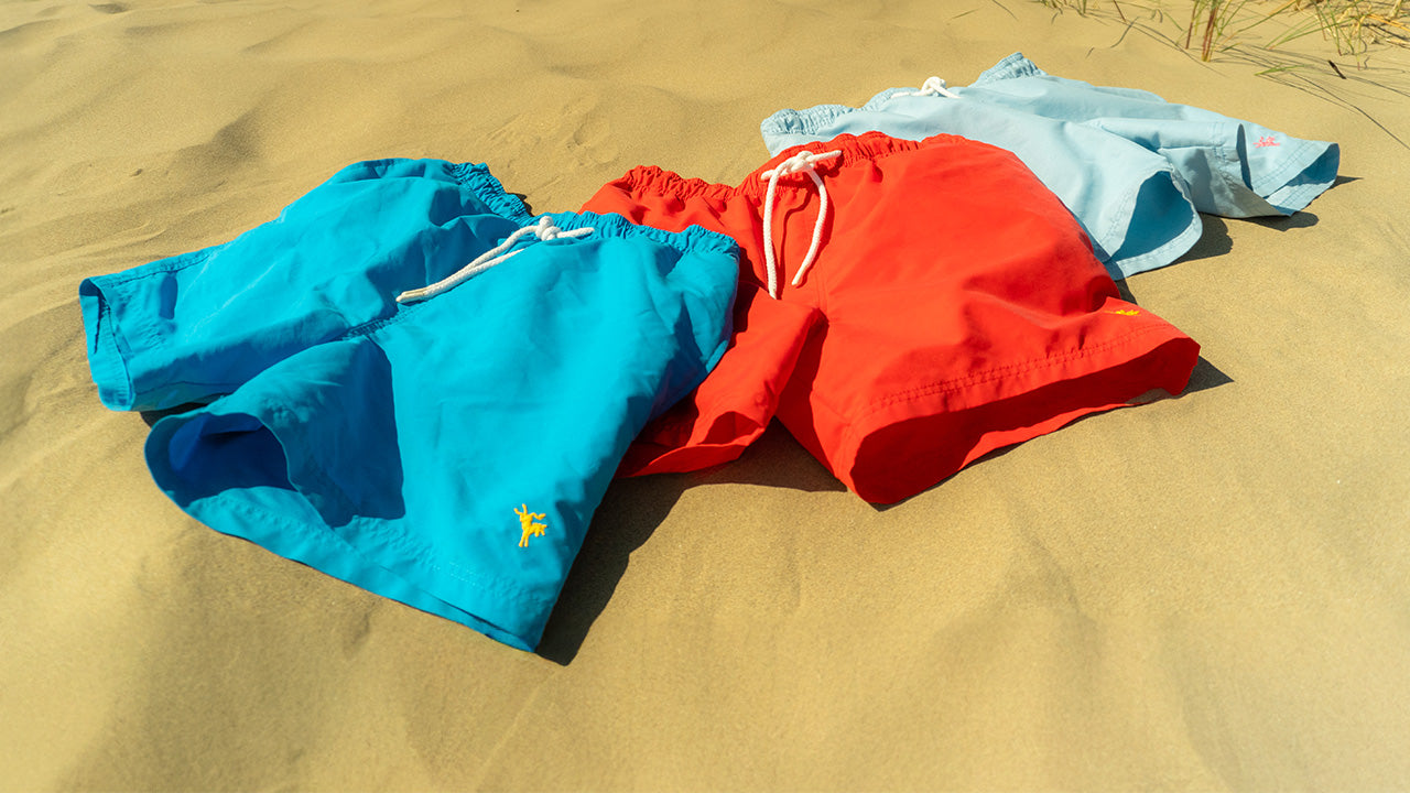 Three pairs of colorful swim shorts on sand