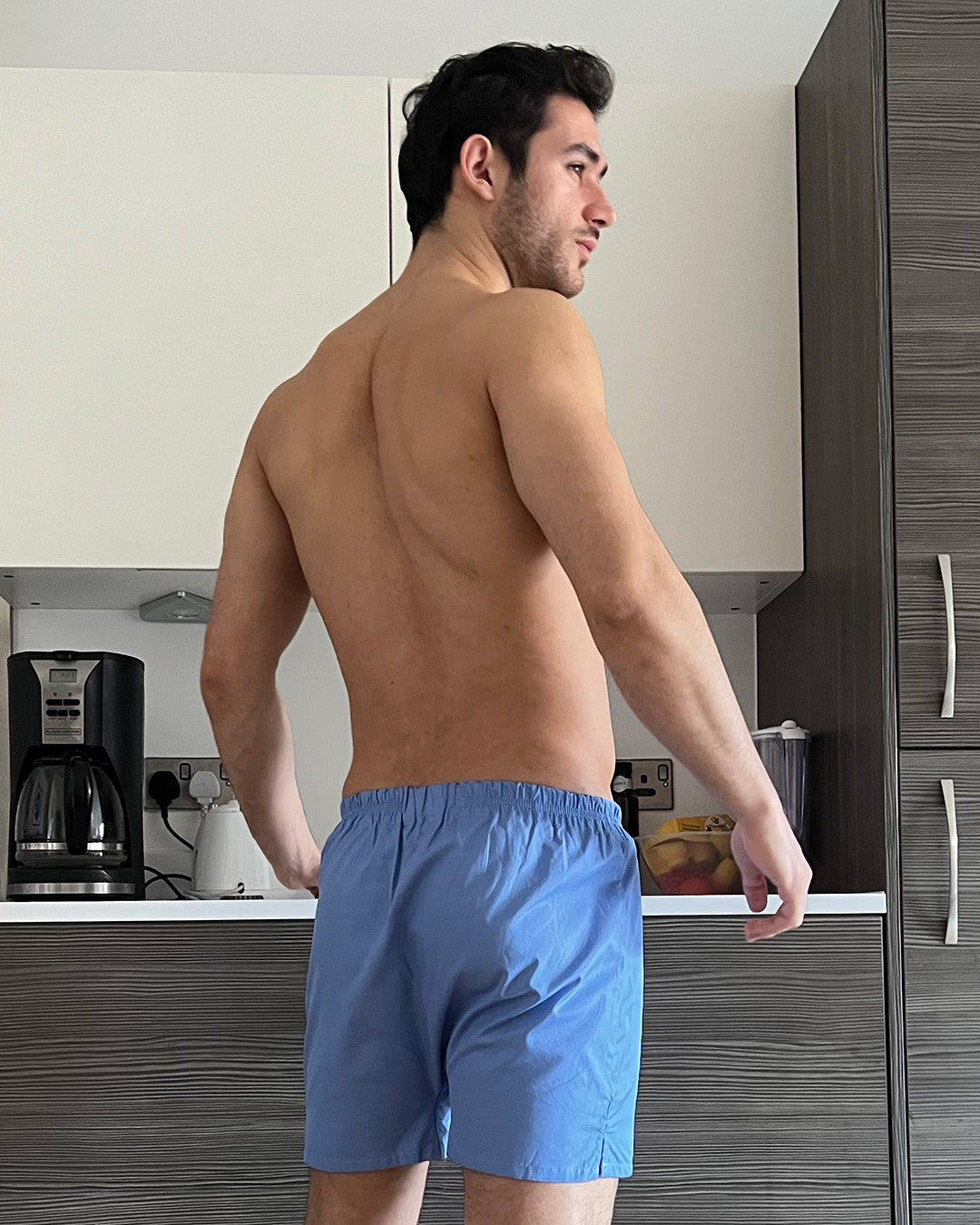 Man wearing blue boxer shorts standing in a kitchen.